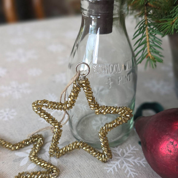 Gold beaded star Christmas decoration propped up against a school milk vase on a Christmas table.