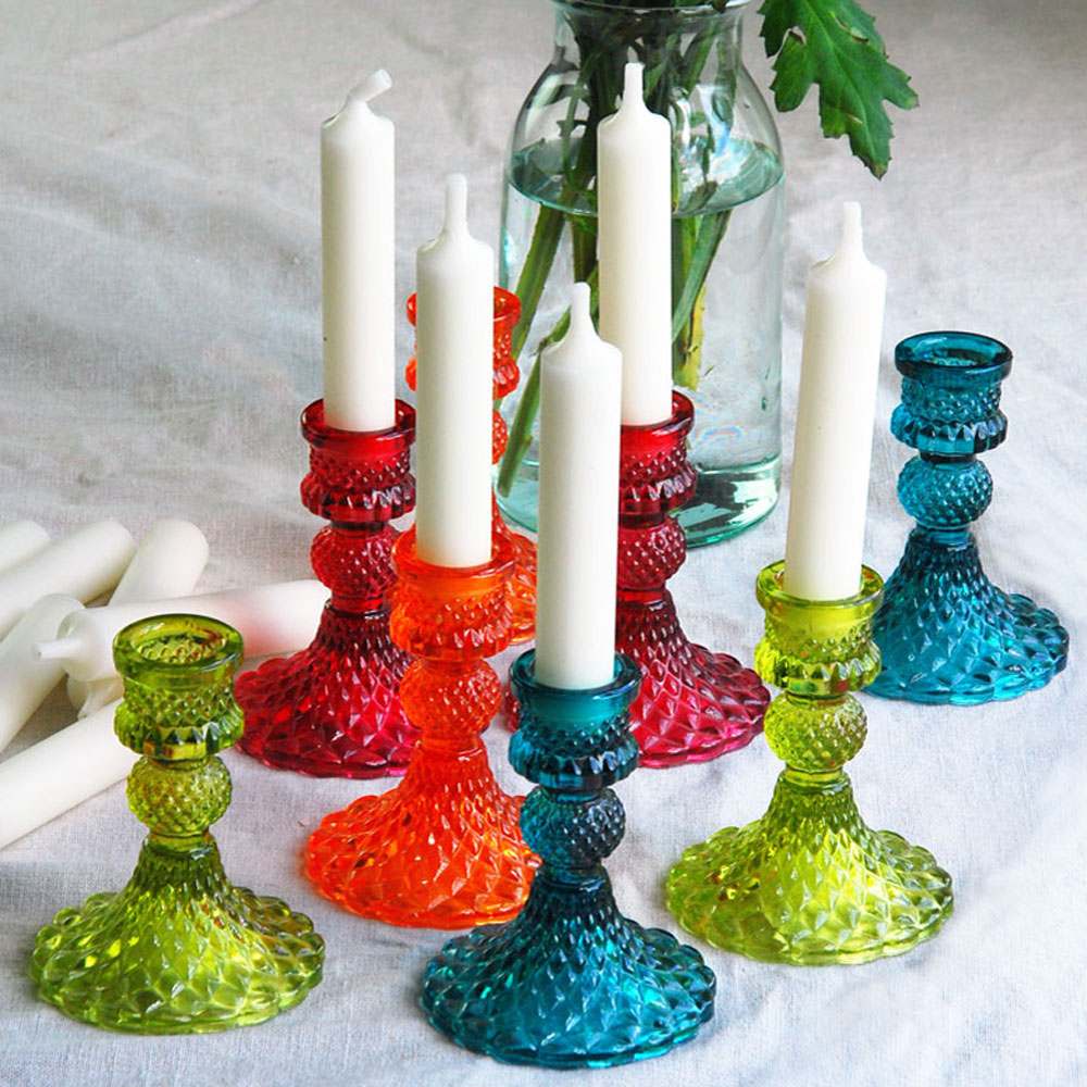 Range of brightly coloured glass candle holders on a linen table cloth