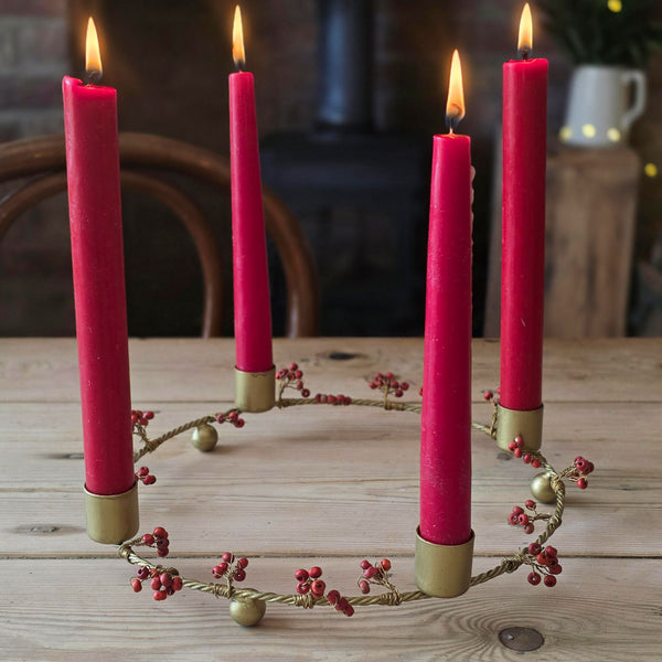 A circular Advent wreath with four lit pink taper candles in gold holders, displayed on a rustic wooden table.