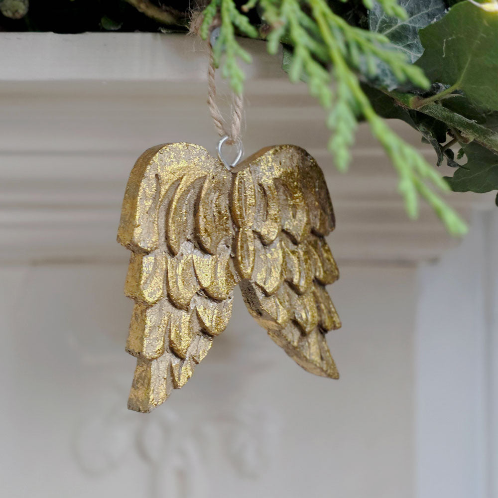 A gold-painted angel wing hanging ornament with a natural jute hanging string, shown hanging in a holiday wreath setting.