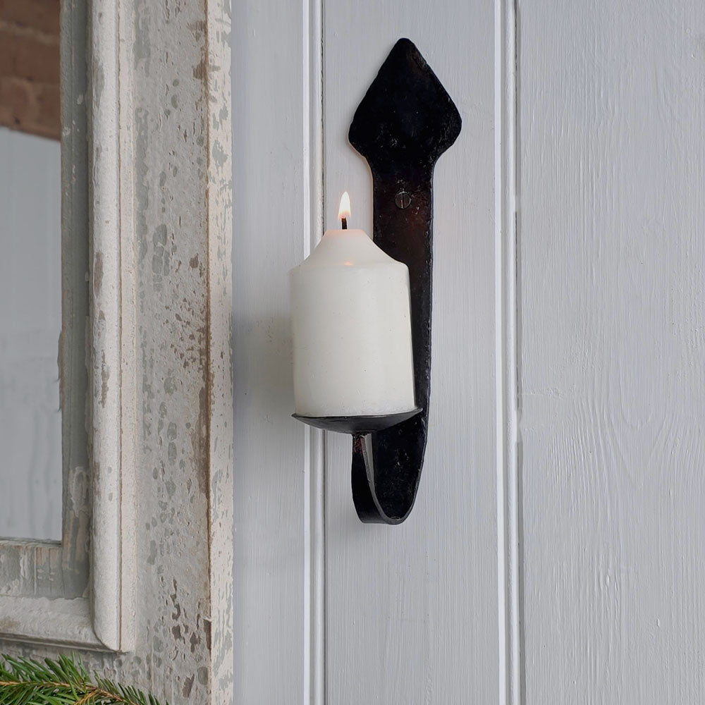 A black metal candle holder mounted on a white paneled door, holding a lit white pillar candle.