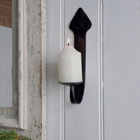 A black metal candle holder mounted on a white paneled door, holding a lit white pillar candle.
