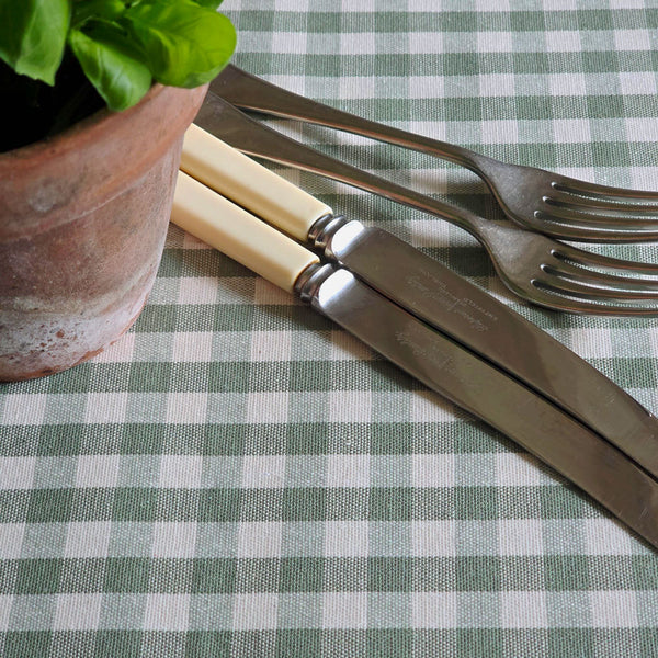 Green gingham wipe clean tablecloth with a potted basil plant and cutlery.