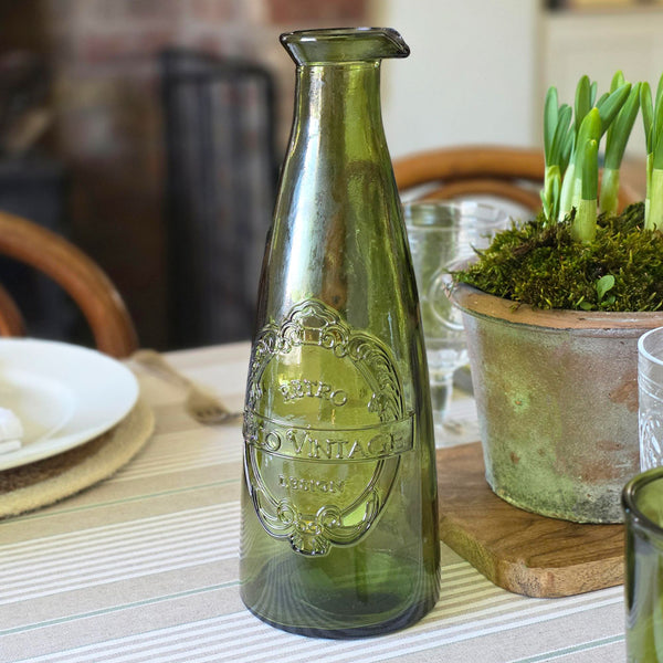 Green glass bottle with decorative label on a table setting