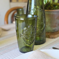 Green glass tumbler and bottle with branding on a table.