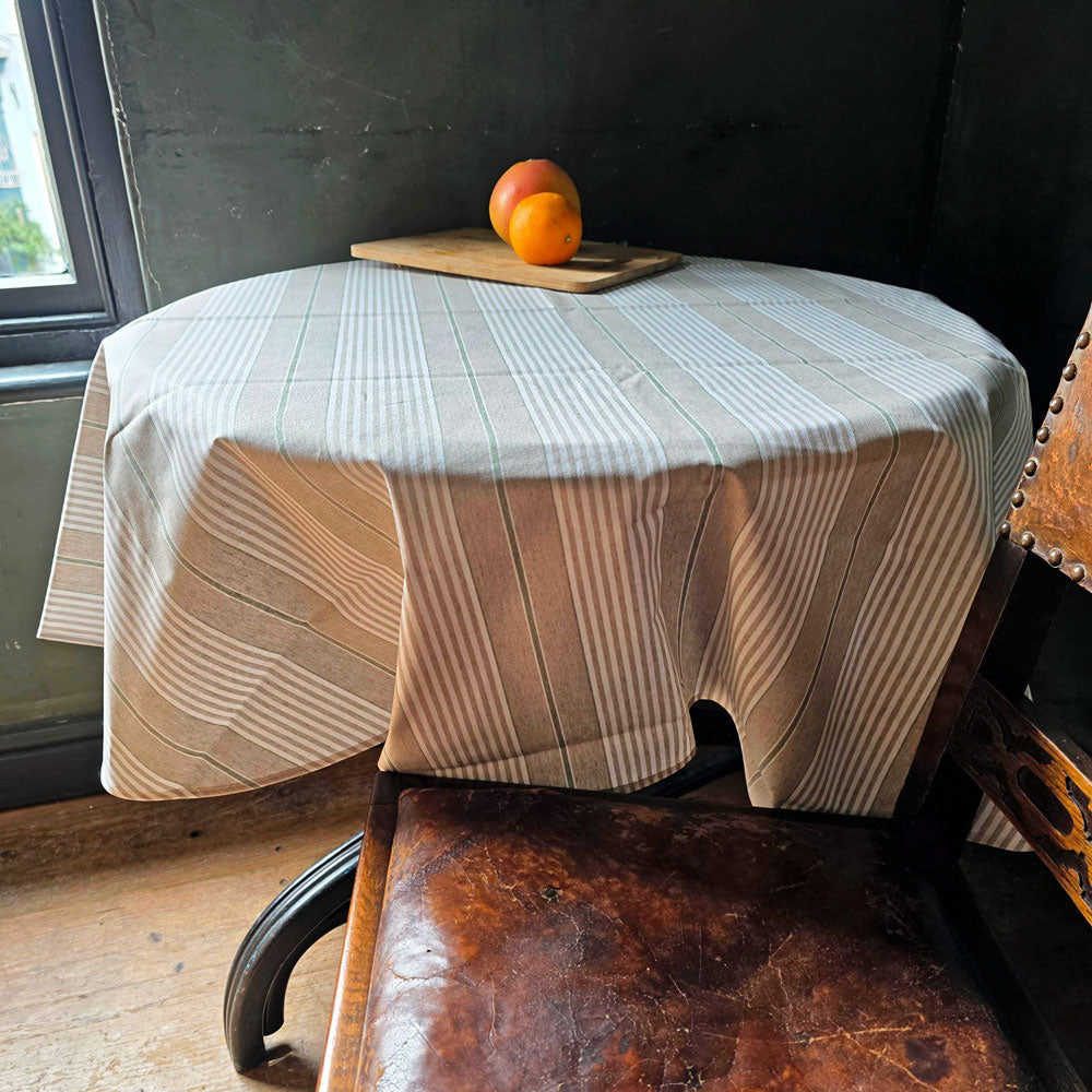 Round table with a striped tablecloth, peaches on a cutting board, and a leather chair in a room.