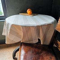 Round table with a striped tablecloth, peaches on a cutting board, and a leather chair in a room.
