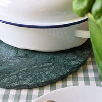 White bowl with blue rim on a green marble serving board over a checkered wipe-clean tablecloth