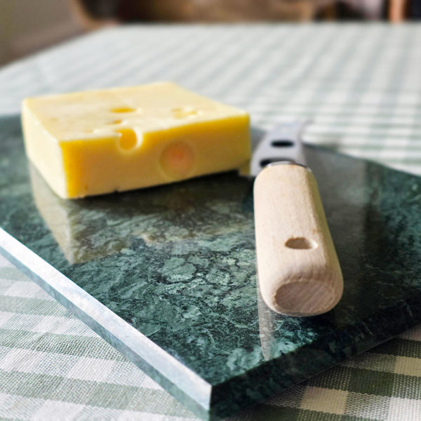 Block of cheese with a knife on a green marble surface