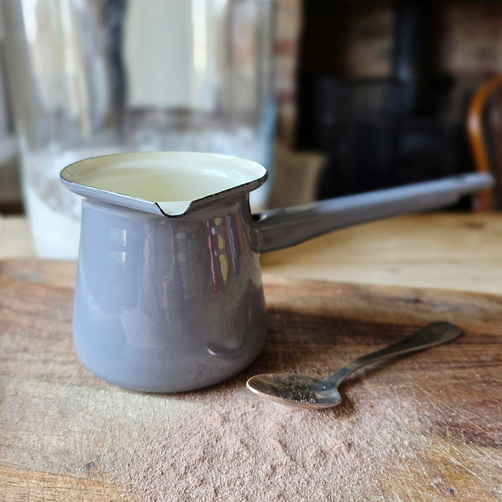 Small slate grey enamel saucepan on a board next to a teaspoon and powdered hot chocolate