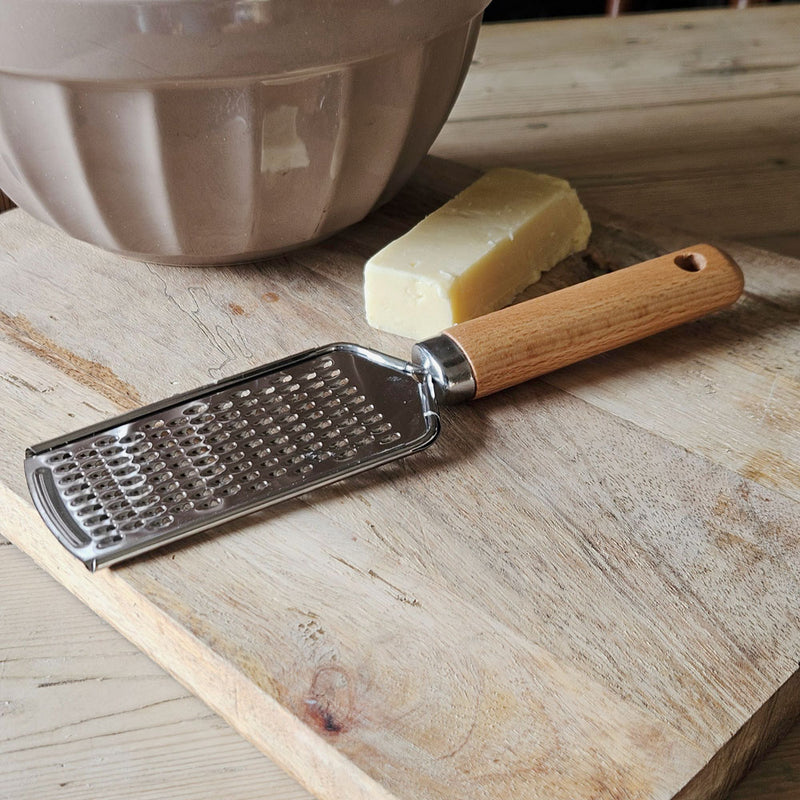 Hand grater on a board with bowl and cheese.