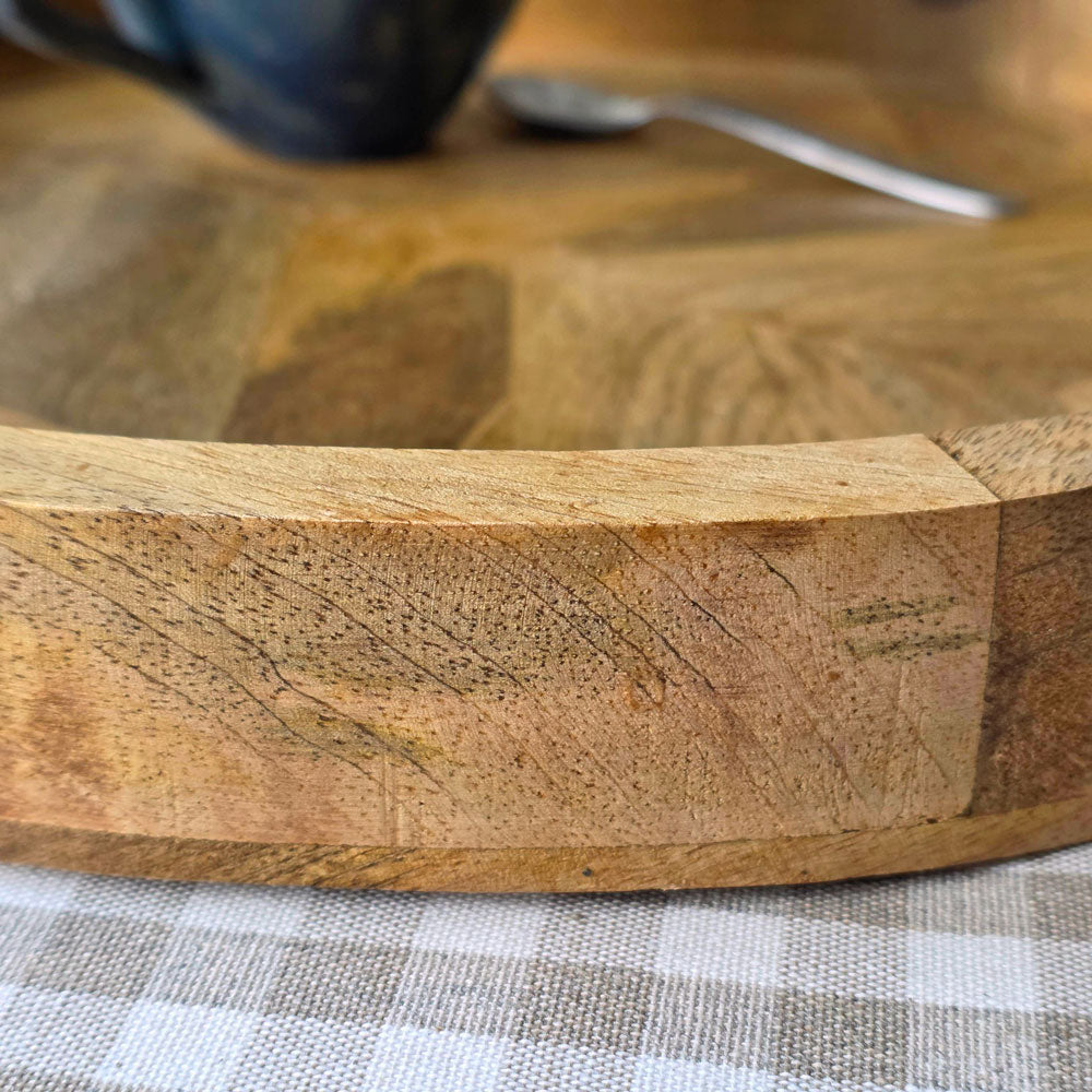 Close up edge of a circular wooden serving tray on a gingham checked tablecloth.