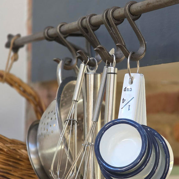 Antique iron kitchen hanging hook rail holding stainless steel and enamel utensils.