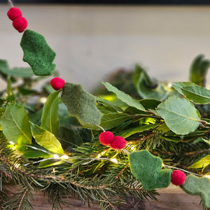 Felt holly berry Christmas garland next to foliage.