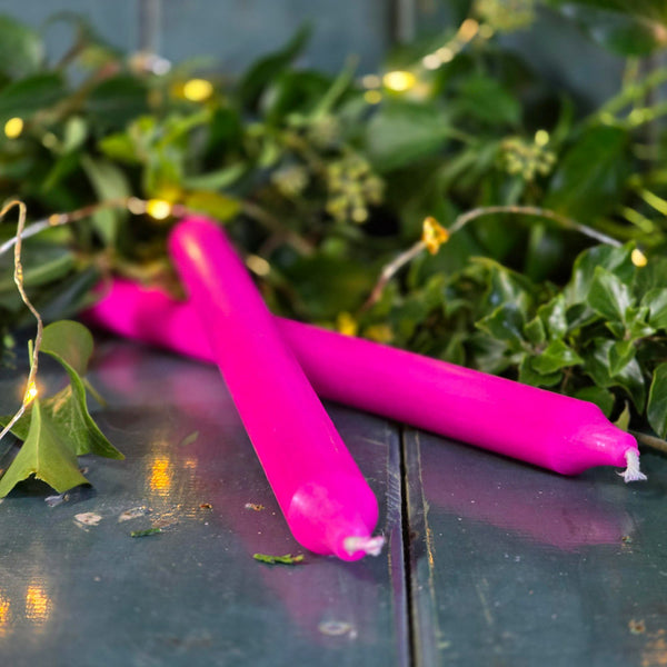 Hot pink Danish dinner candle on a teal wooden surface, next to Christmas foliage and lights.