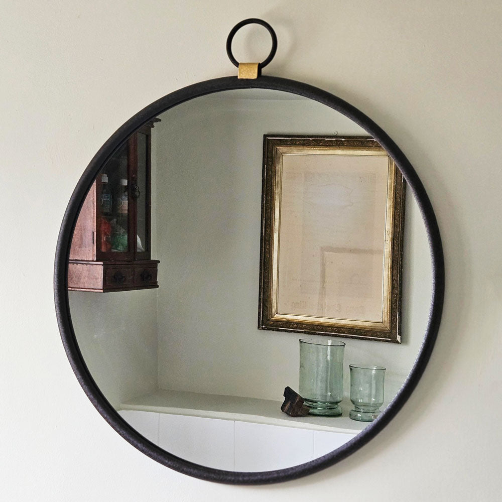 Round wall mirror with black frame hanging on a white wall