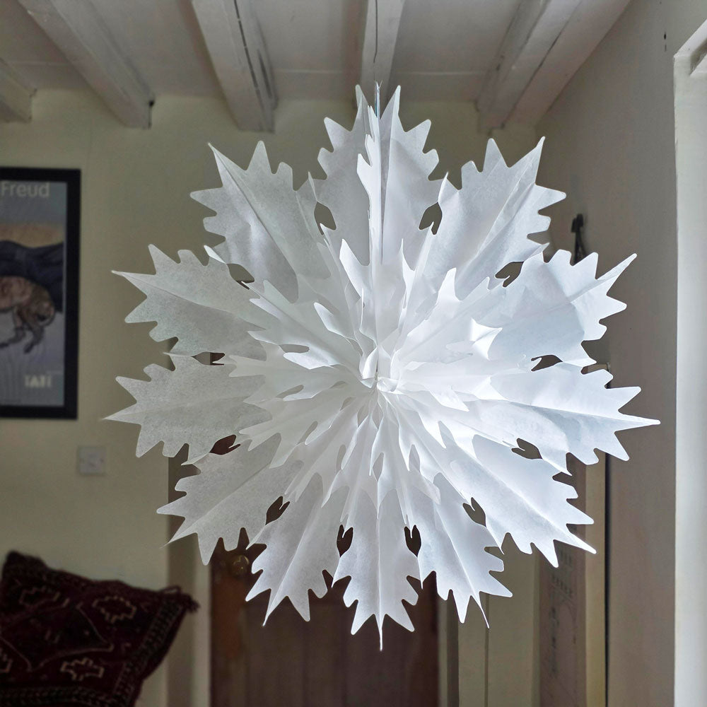 Giant white tissue paper snowflake hanging in a window.