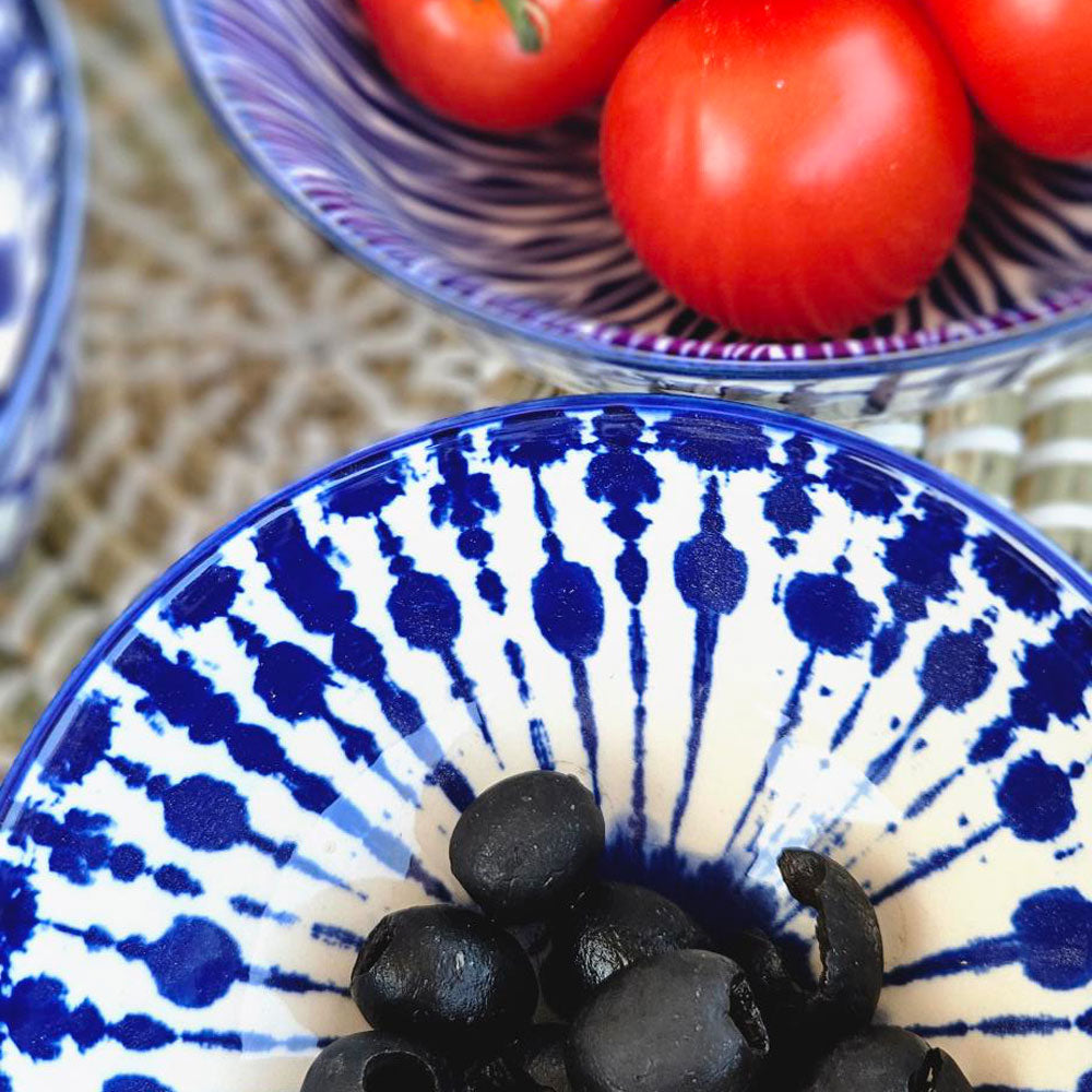 Blue and white patterned bowl with black olives and red tomatoes on a woven surface