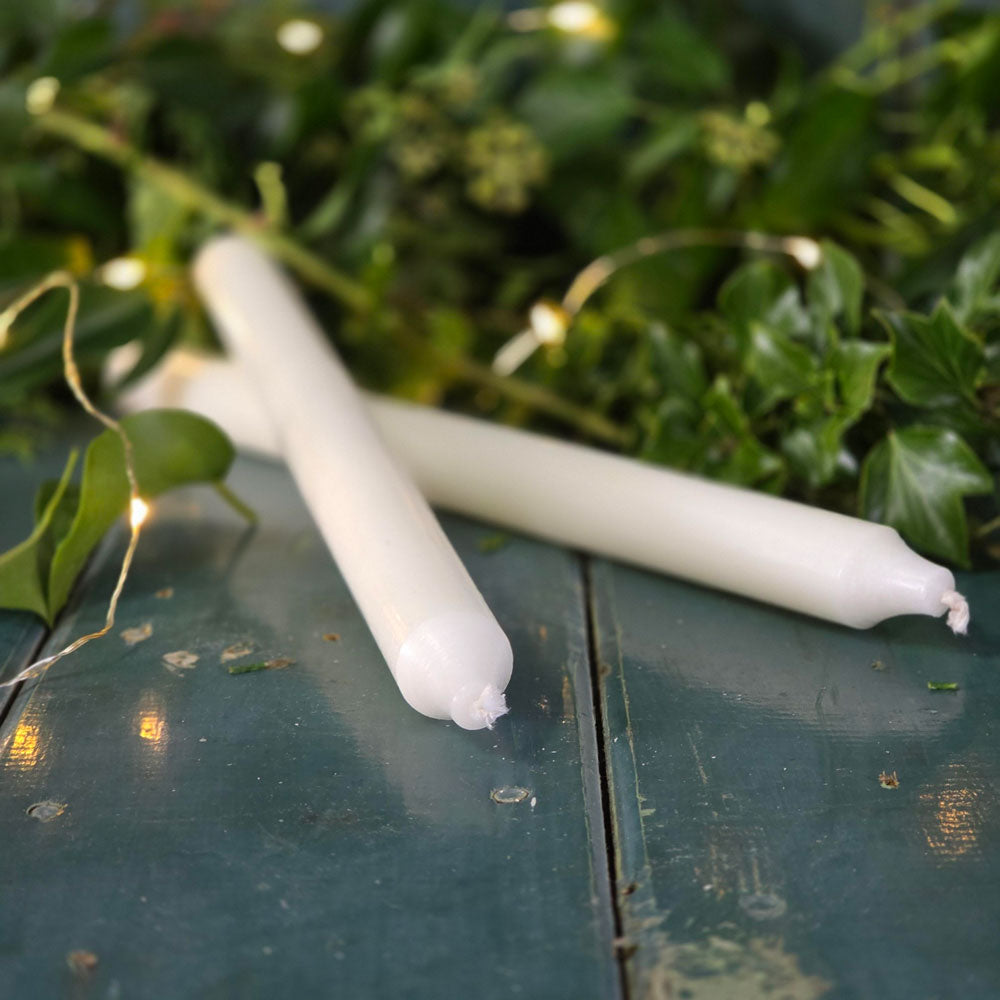 Ivory Danish dinner candles on a blue surface surrounded by foliage and fairy lights.