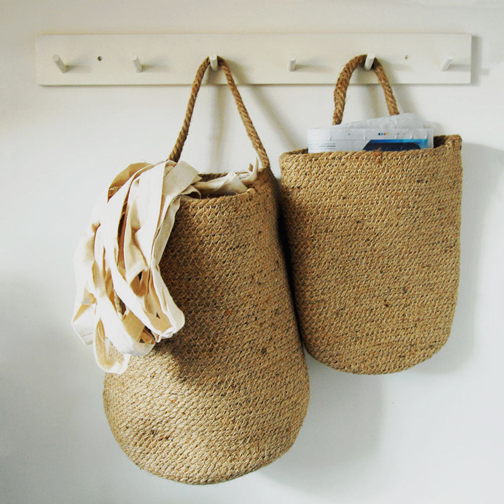 Jute storage baskets filled with recycling materials hanging from a peg rail.
