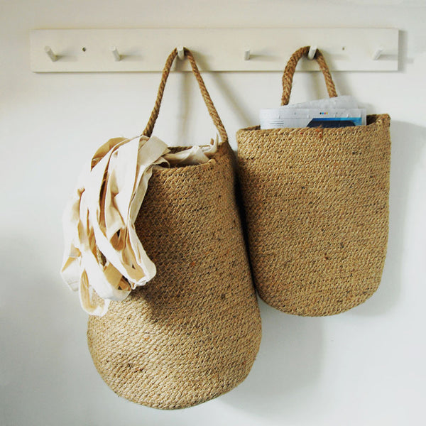Jute storage baskets filled with recycling materials hanging from a peg rail.