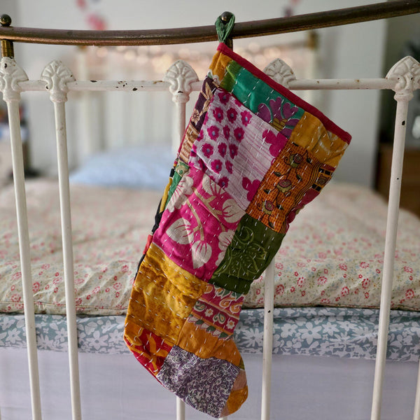 Kantha sari patchwork Christmas stocking hanging from an iron bed.