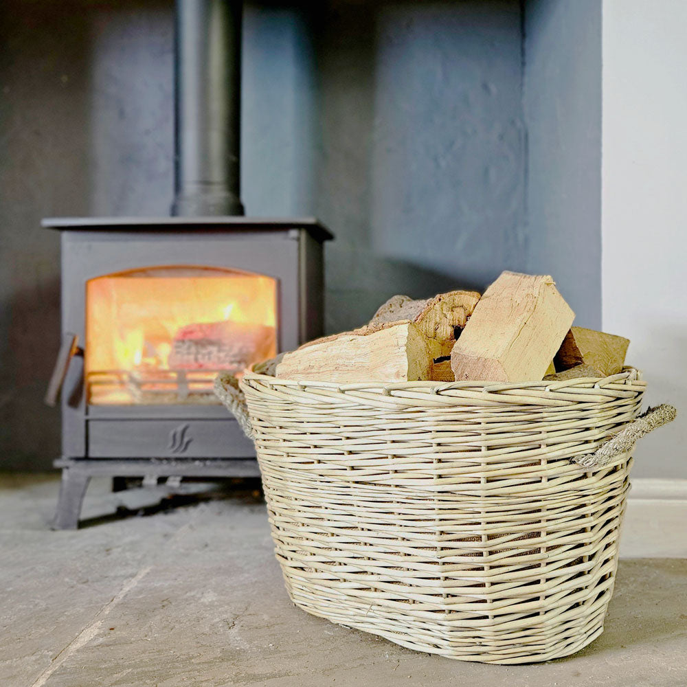 Large val wicker log basket on a hearth next to a lit wood burning stove