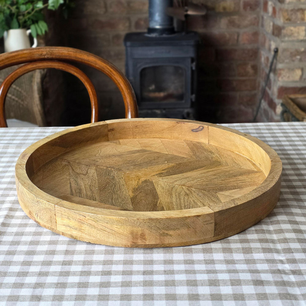Round wooden serving tray with herringbone pattern base on a gingham checked tablecloth.