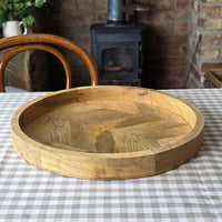 Round wooden serving tray with herringbone pattern base on a gingham checked tablecloth.