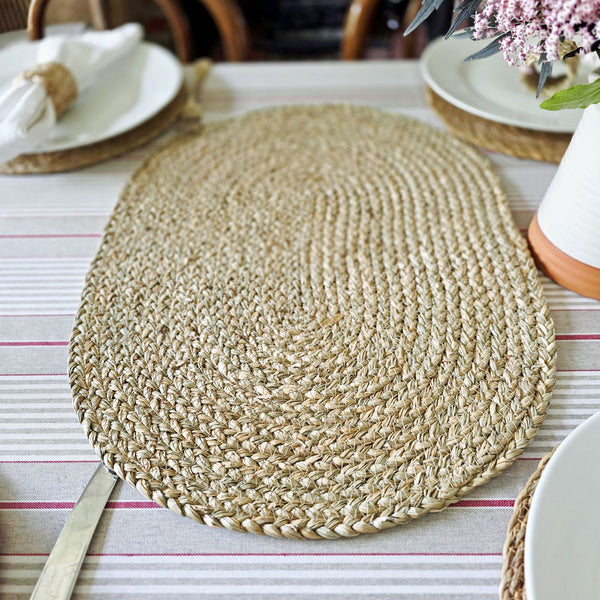 Large oval seagrass placemat on the centre of a table covered with red striped tablecloth set for serving.
