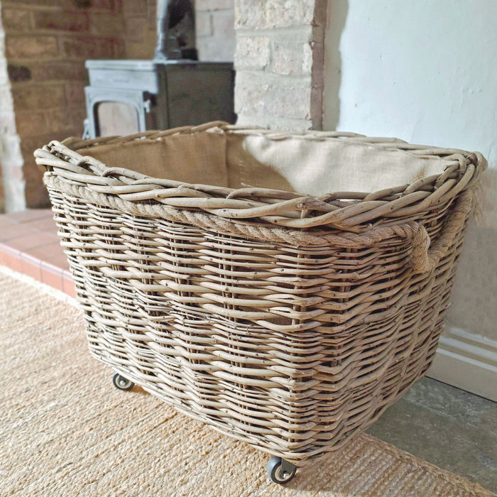 Wicker log basket with wheels on a carpeted floor.