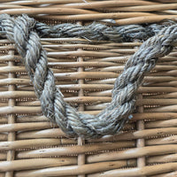 Close-up of a thick, twisted gray rope handle resting on a light brown woven wicker basket.