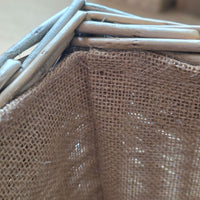 Close-up detail of a woven basket made from natural light brown wood and tan burlap fabric.