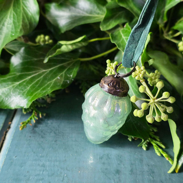 Decorative green ornament hanging among green leaves and plants on a wooden surface.