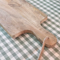 Mango wood charcuterie board on green gingham tablecloth.