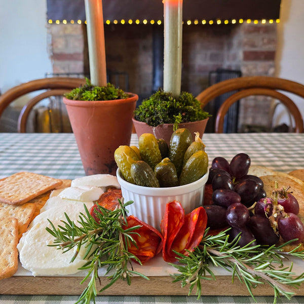 Platter of assorted cheeses, crackers, pickles, and grapes with a candlelit background.