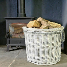 Round white wicker log basket filled with logs next to a lit wood burning stove.