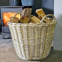 Traditional round wicker log basket filled with cut logs next to a lit log burner.