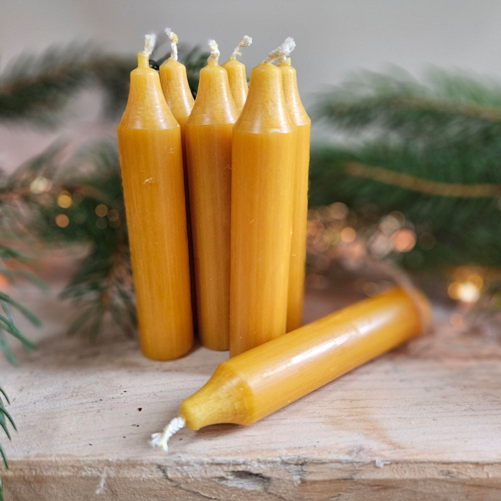 Hand made danish candles in mustard on a shelf covered with Christmas foliage.