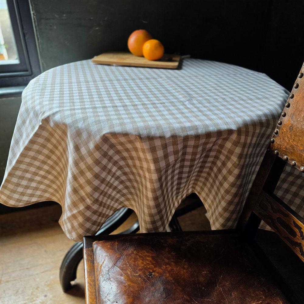 Round natural gingham checkered wipe clean tablecloth next to a leather chair