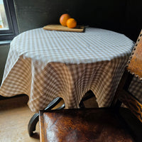 Round natural gingham checkered wipe clean tablecloth next to a leather chair