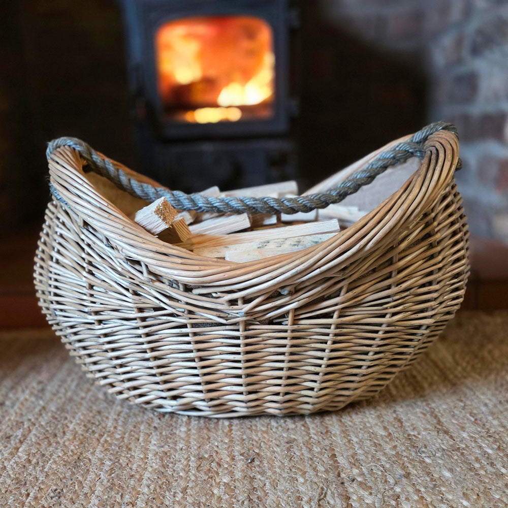 Wicker boat shaped log basket filled with kindling next to a lit stove