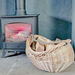 Oval Oakham wicker kindling basket on a hearth next to a lit wood burning stove.