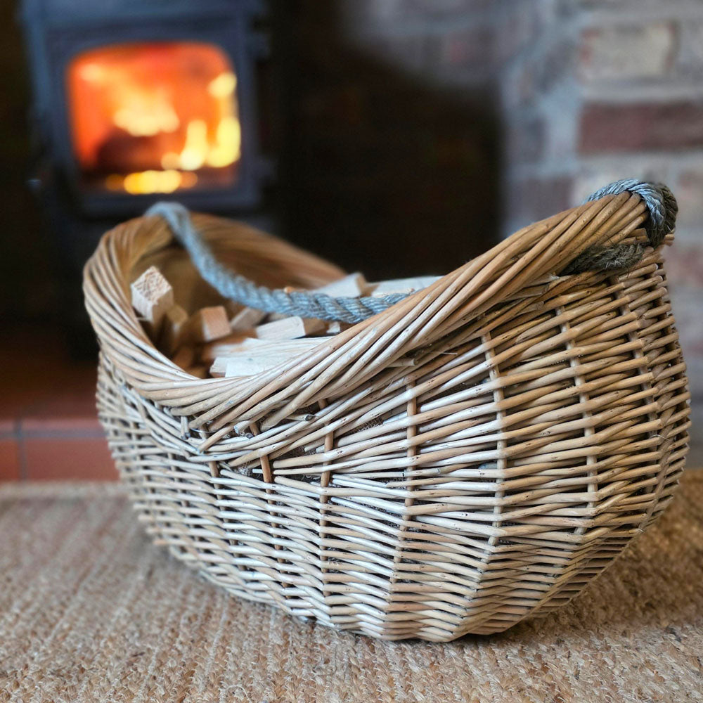 Side view of wicker log and kindling basket next to a lit stove.