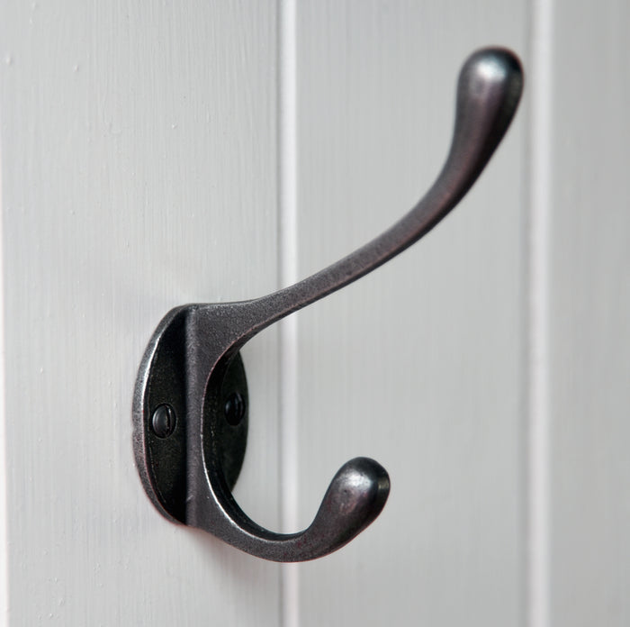A black Oakham coat hook made from cast metal, mounted on a white wall.