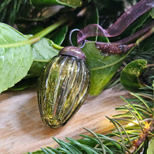 Green glass pine cone shaped Christmas bauble amongst foliage