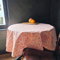A circular orange coral wipe clean tablecloth with oranges on a table