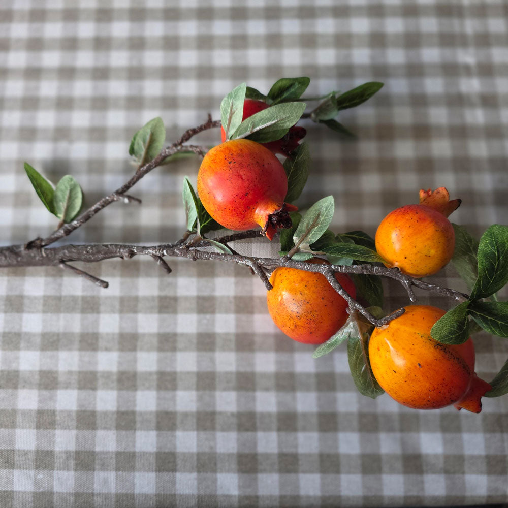 Orange faux pomegranate branch on a beige gingham checked tablecloth.