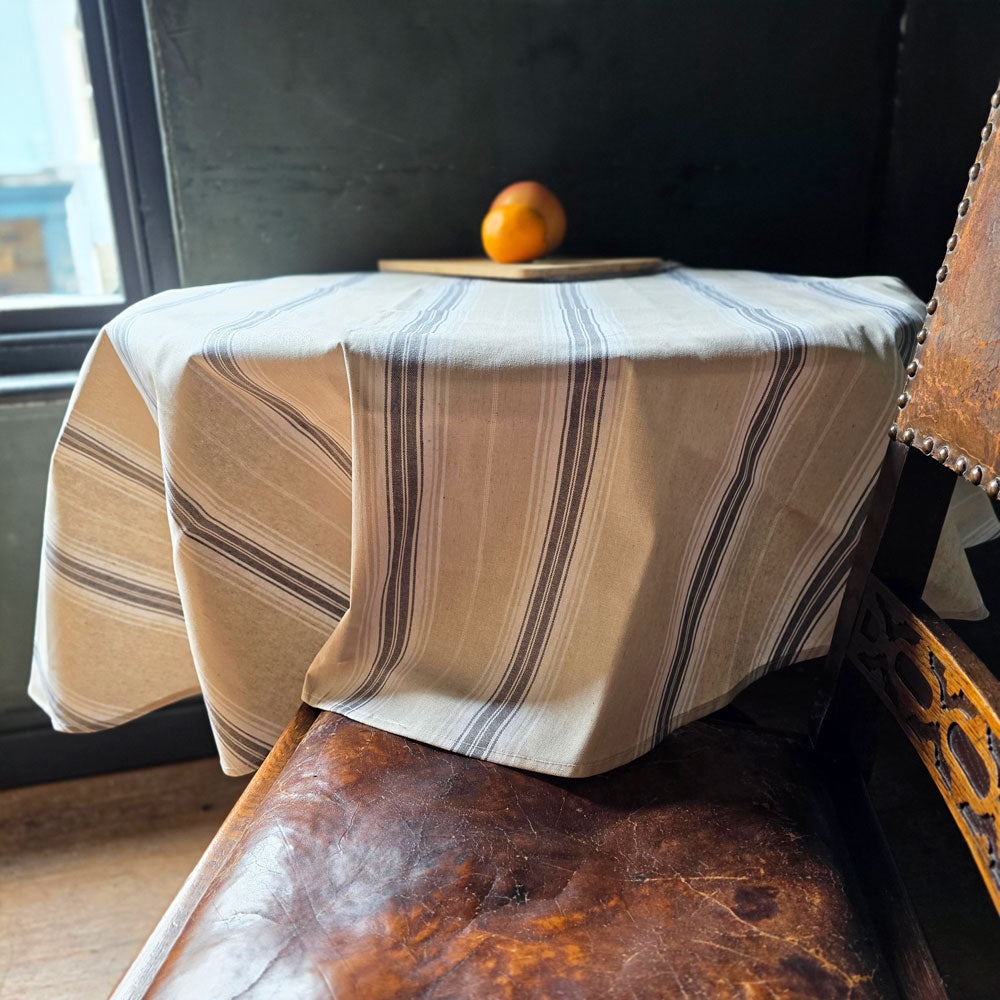 Striped tablecloth on a wooden table with an orange in a room with a window.