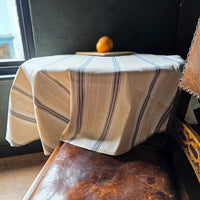 Striped tablecloth on a wooden table with an orange in a room with a window.
